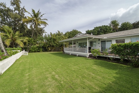 Charming tropical cottage with covered porch surrounded by lush greenery and swaying palm trees in a peaceful residential setting.
