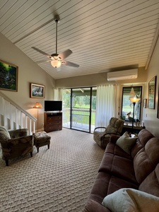 Sink into plush seating and unwind in your spacious living room, where vaulted ceilings and a private balcony overlooking lush greenery create the perfect escape for relaxation.