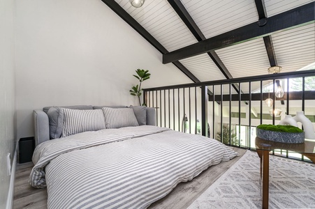 Drift off in your loft bedroom featuring crisp striped linens and exposed beams that frame peaceful garden views.