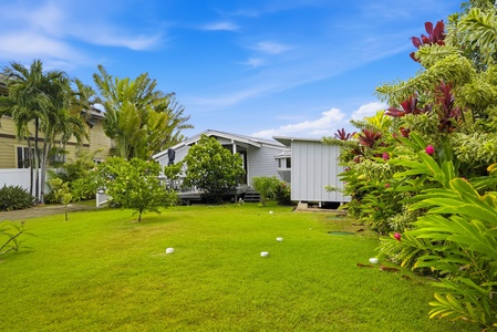 Charming vacation property surrounded by vibrant tropical gardens featuring palms, colorful flowers, and a lush green lawn under clear blue skies, providing a peaceful island retreat.
