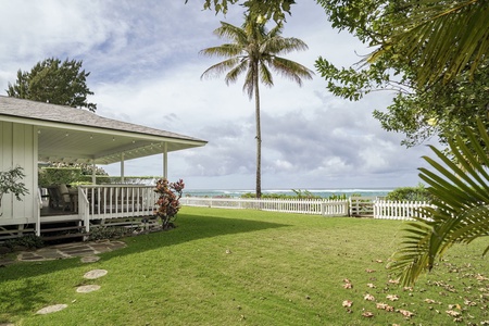 Beachfront tropical paradise with lush lawn, swaying palms, and ocean views just beyond the white picket fence.