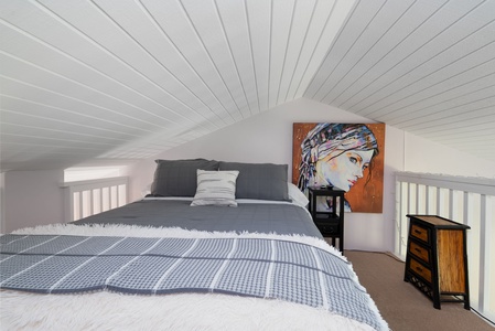 Sink into this cozy loft bedroom where soft textures and unique artwork create your peaceful retreat under charming wood-paneled ceilings.