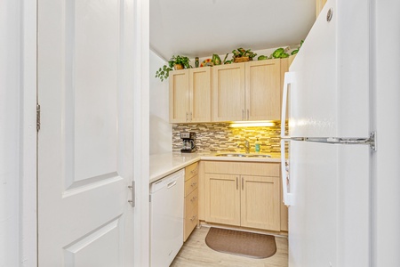 Your fully equipped kitchen awaits with warm wood cabinets, modern appliances, and charming plants above—perfect for preparing meals during your stay.