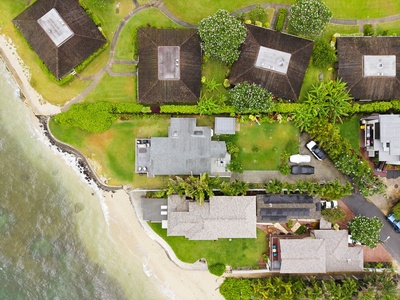 An aerial view showcasing a beachfront property nestled among lush tropical greenery, with neighboring homes and winding roads framing the serene coastal setting.