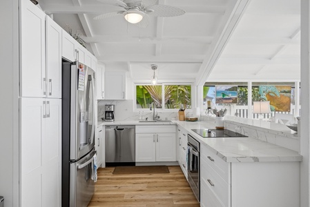 Sleek white kitchen with marble counters, stainless appliances, and tropical greenery framed by your windows—your culinary retreat awaits.