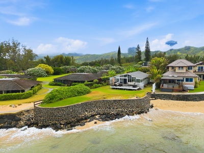 Aerial view of beachfront homes nestled between sandy shores and lush mountain foothills, offering direct beach access and tropical island tranquility.