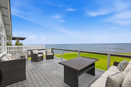 Picture yourself sipping morning coffee on this expansive waterfront deck. Comfortable seating frames stunning sea views across manicured lawns, creating your perfect coastal retreat under open skies.