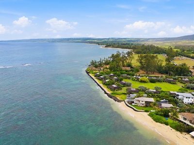 Aerial view of beachfront community nestled along pristine shores, surrounded by lush greenery and rolling hills, offering tranquil coastal access and scenic natural beauty.