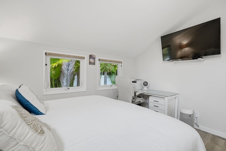 Unwind in your bright, airy bedroom with crisp linens, a dedicated workspace, and a wall-mounted TV for your entertainment. Tropical greenery just outside the windows adds a refreshing touch to your stay.