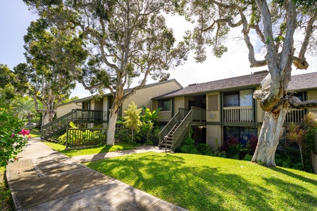 The property's two-story residential buildings are nestled beneath mature shade trees, with lush lawn and landscaped gardens creating a peaceful, park-like setting.