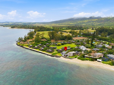 Aerial view showcasing the property's beachfront location in a tranquil coastal neighborhood, surrounded by lush greenery and sweeping mountain vistas.