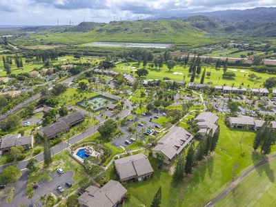 Aerial view of tropical resort nestled amid lush golf course greens, with mountains and rolling hills forming a stunning backdrop.