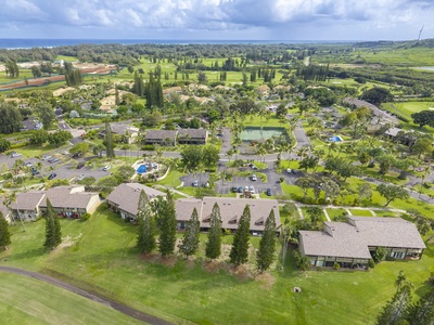 Aerial view of a tropical resort property nestled among lush greenery with golf course and ocean views in the distance.