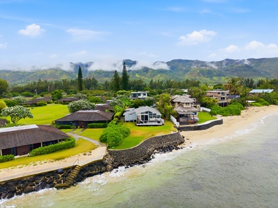 Beachfront property nestled between sandy shores and lush mountain peaks wrapped in morning clouds, offering a serene coastal neighborhood setting.