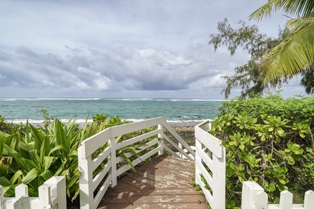 Charming wooden walkway leads through tropical gardens to pristine beachfront, where turquoise waters and palm-fringed shores create your perfect island escape.