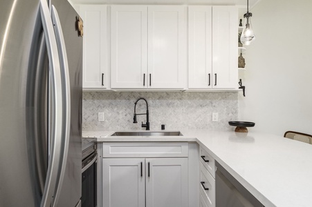 Cook in your modern kitchen with white cabinetry, herringbone backsplash, and stainless steel appliances creating a clean, welcoming space.