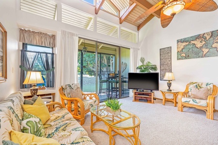 Unwind in your tropical-themed living room with bamboo furnishings, ceiling fan, and peaceful patio views through sliding doors.