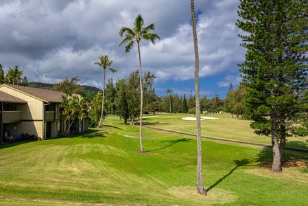 The property is located adjacent to a lush golf course surrounded by towering palms, tropical greenery, and rolling mountains under dramatic island skies.