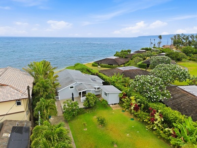 Aerial view of a coastal property nestled in a lush tropical neighborhood with expansive ocean views and vibrant gardens, located in a serene beachfront community.