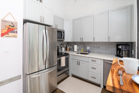 Your fully equipped kitchen features modern stainless appliances, sleek white cabinetry, and stylish subway tile backsplash—ready for preparing meals and morning coffee in comfort.