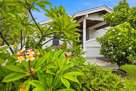 A charming coastal cottage framed by lush tropical landscaping with vibrant plumeria and fragrant blooms welcoming guests to your island retreat.