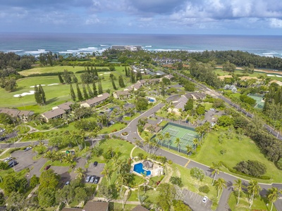 Aerial view of tropical vacation community featuring oceanfront location, tennis court, swimming pool, and golf course surrounded by lush landscaping.