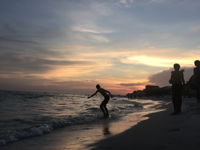 Beach activities unfold beneath a spectacular sunset, with golden clouds painting the sky over gentle waves and sandy shores.