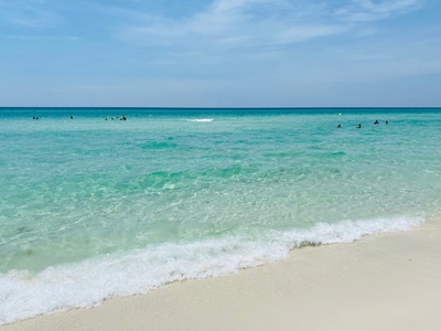Pristine white sand beach with crystal-clear turquoise waters where guests enjoy swimming in the gentle waves.