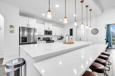Your sleek modern kitchen features pristine white countertops, stainless steel appliances, and elegant pendant lighting perfect for cooking memorable meals.