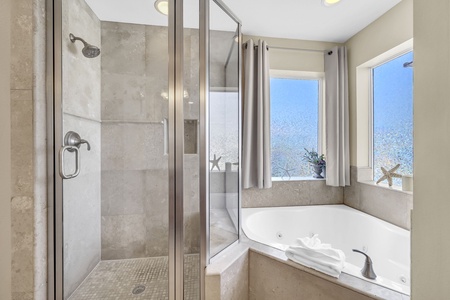 Unwind in your serene bathroom retreat, where a luxurious soaking tub awaits beside windows framing peaceful views. The spacious glass-enclosed shower and coastal-inspired touches create your perfect sanctuary.