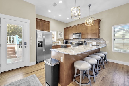 Gather around your fully equipped kitchen island with seating for four, featuring granite countertops, modern appliances, and warm wood cabinetry bathed in natural light.
