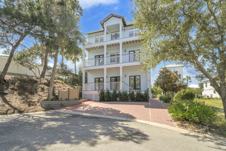 A charming three-story coastal vacation home nestled among mature trees and lush landscaping, offering a peaceful retreat with spacious balconies and convenient driveway parking for your arrival.