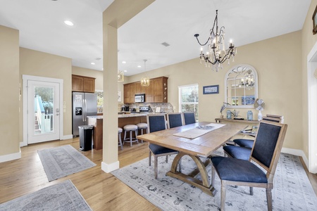 Gather around this elegant dining table where the open layout invites easy conversation with the chef. Soft natural light streams through the windows as the chandelier above creates a warm, welcoming glow for your meals.