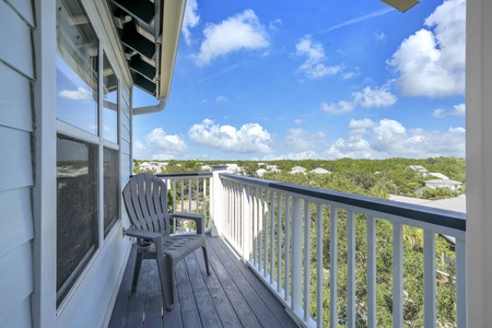 The property overlooks a lush, tree-filled coastal area with neighboring homes nestled among natural greenery and blue skies overhead.
