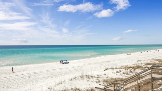 Pristine white sand beach with turquoise waters and wooden boardwalk access, perfect for peaceful coastal getaways.