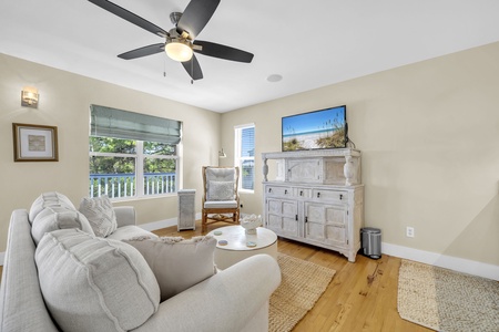 Unwind in your bright, airy living room with soft coastal tones, a cozy sectional, and a charming rocking chair—perfect for lazy mornings or evening relaxation after a day at the beach.