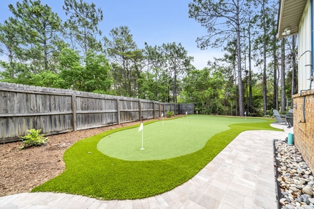 Private backyard oasis featuring a custom putting green surrounded by lush pines and mature trees!