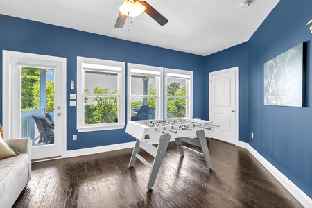 Challenge friends to a game of foosball in this vibrant blue game room, where natural light streams through large windows overlooking lush greenery outside.
