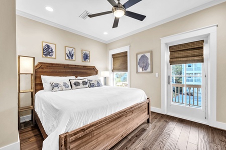 Your coastal bedroom features rich wood floors, a rustic bed with ocean-themed pillows, and French doors opening to your private balcony.
