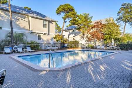 Refreshing community pool with lounge chairs surrounded by mature trees and residential buildings.