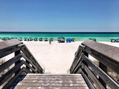 Steps from boardwalk to pristine white sand beach with turquoise waters and beach umbrellas.