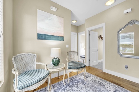 Sink into elegant vintage chairs in your private sitting area, where coastal artwork and warm wood floors create a refined, welcoming retreat.