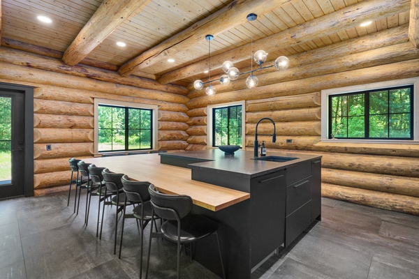Modern meets rustic in this cabin's kitchen, featuring a spacious island dining table/bar seating surrounded by natural wood—a perfect blend for entertaining.