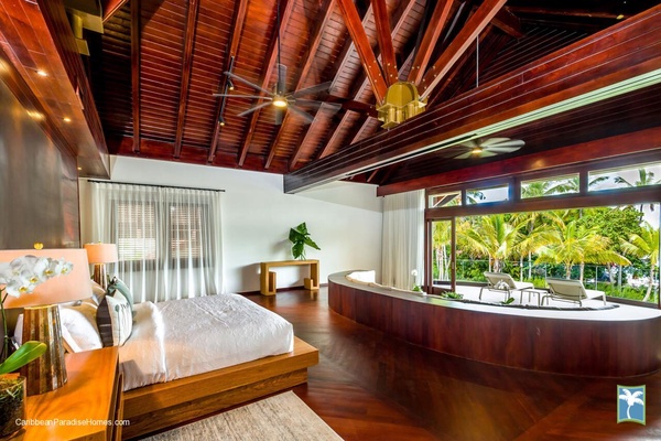 Spacious primary bedroom with a curved sofa and garden view.