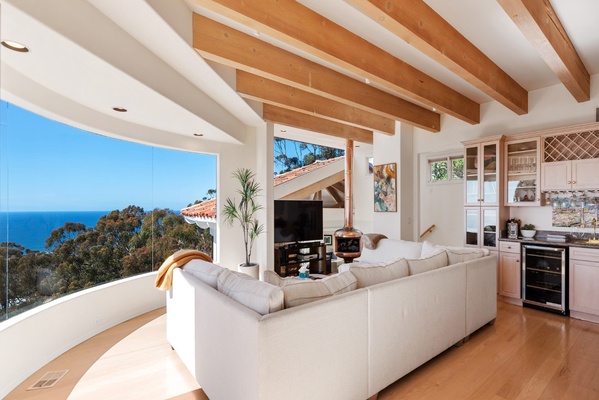 Living room with plenty of sofa seating, smart tv and copper fireplace open to primary bedroom high beams.