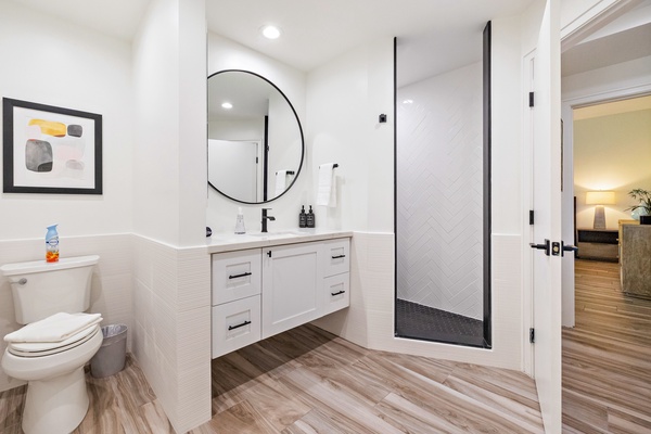 This sleek and modern bathroom offers a clean design with a round mirror, contemporary black fixtures, and a spacious vanity.