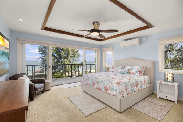 Primary bedroom with Tempur-Pedic California king bed, see-through fireplace, split air conditioning, and lanai with a view of the pool and ocean.