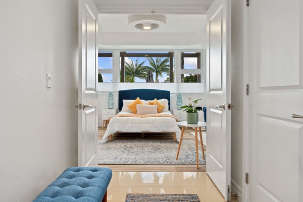 Step into the serene Primary Suite with gleaming hardwood floors leading towards a cozy bed, framed by a stylish blue headboard.