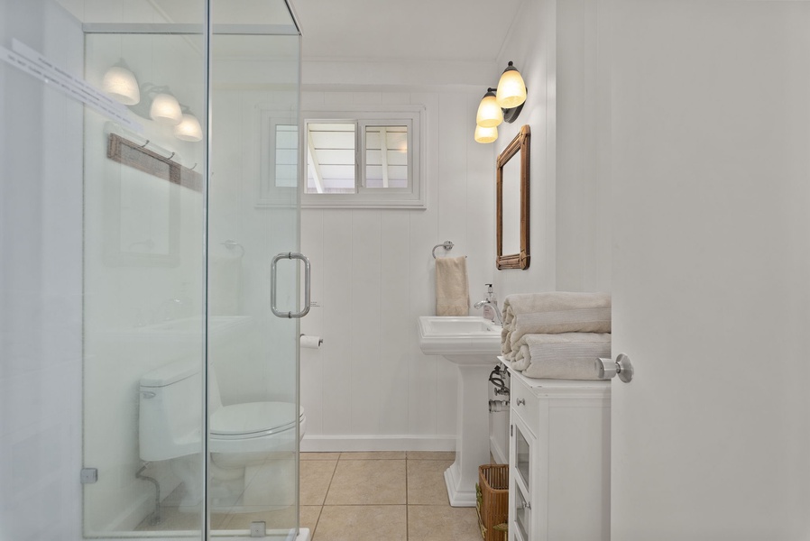 Step into your bright, modern bathroom featuring a spacious glass shower and pristine white vanity with fresh towels awaiting your arrival.