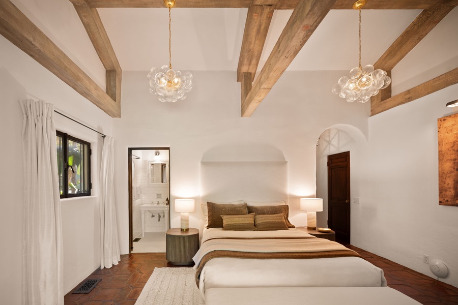Sleep easy under wood beams and soft chandeliers in this peaceful main bedroom with garden views and a spa-like bath.